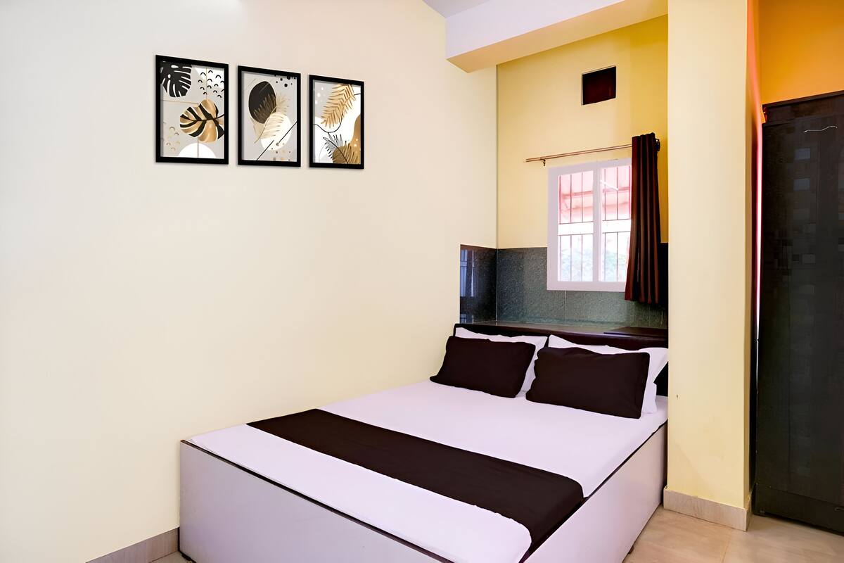 A bedroom with a bed, a window with curtains, and three framed artworks on the wall.