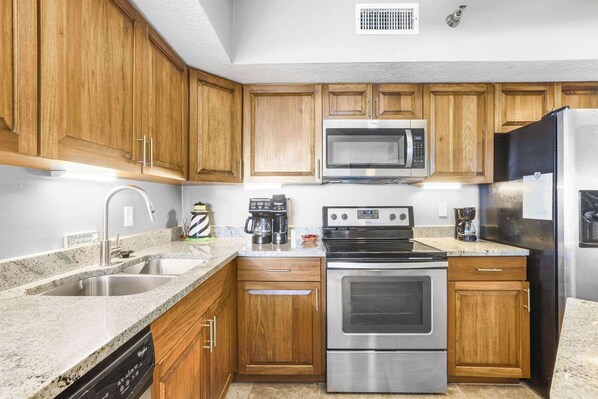 A kitchen with wooden cabinets, stainless steel appliances, a dishwasher, and granite countertops.