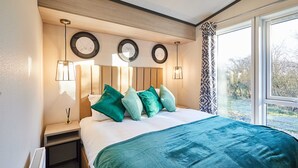 Ein Hotelzimmer mit einem großen Bett, einem Nachttisch, einer Wandlampe und einem Fenster mit Blick auf Bäume.