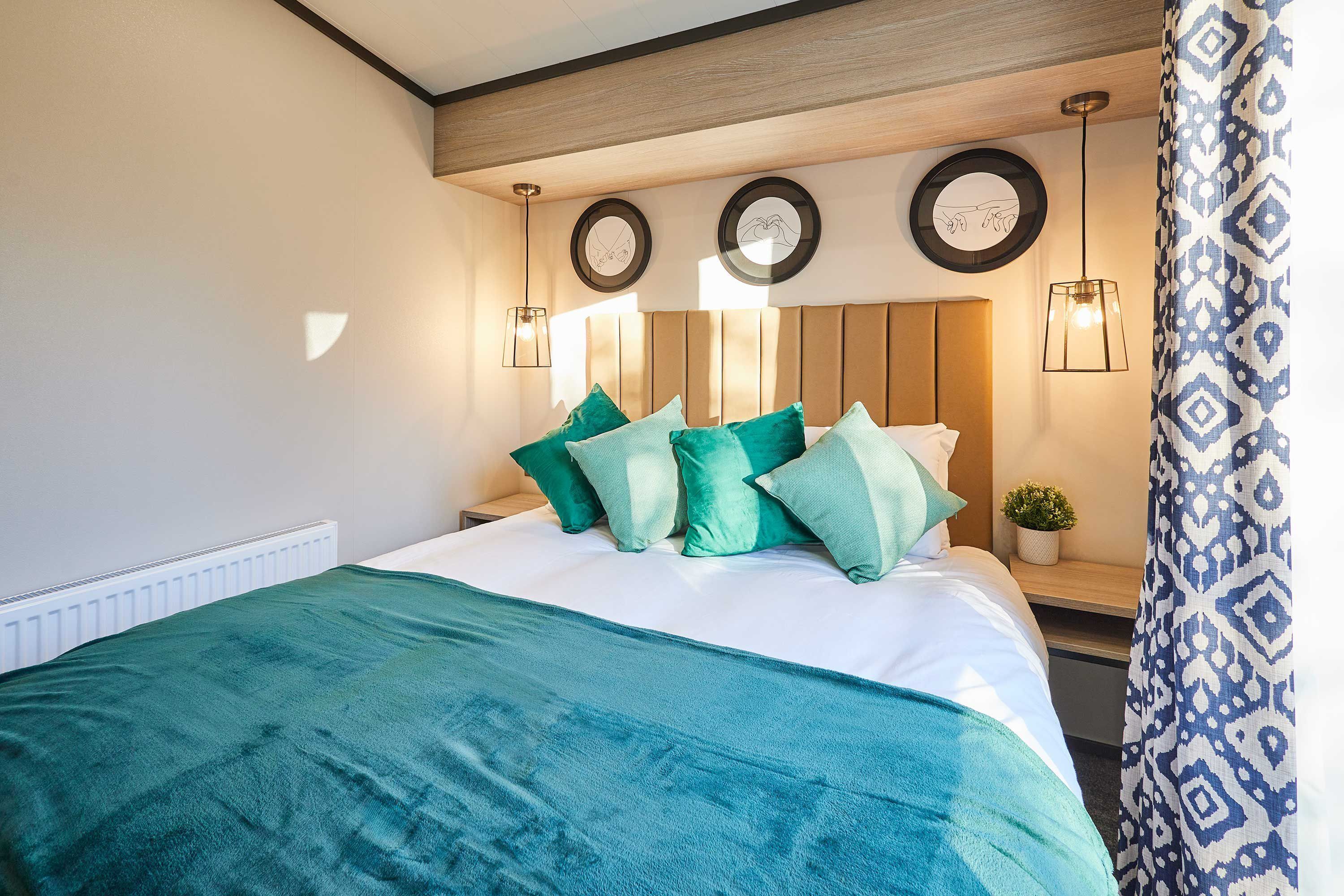 Un dormitorio con una cama, almohadas verdes, cabecero de madera, dos espejos circulares montados en la pared y una cortina estampada.