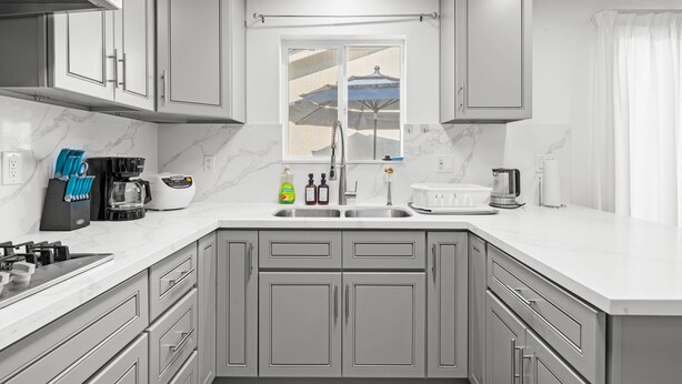 A modern kitchen with grey cabinets, a white countertop, and a window with a view of a beach. - Comfy Retreat With Yard Cozy Interiors (San Gabriel)