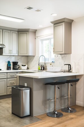A modern kitchen with a central island, bar stools, stainless steel appliances, and marble countertops. - Comfy Retreat With Yard Cozy Interiors (San Gabriel)