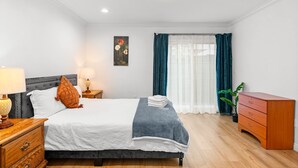 A neatly arranged bedroom with a bed, bedside tables, a dresser, and a window with curtains. - Comfy Retreat With Yard Cozy Interiors (San Gabriel)