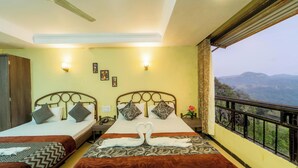 A hotel room with two beds, a balcony with a view of the mountains, and a ceiling fan. - Indira Nature Valley (Mahabaleshwar)