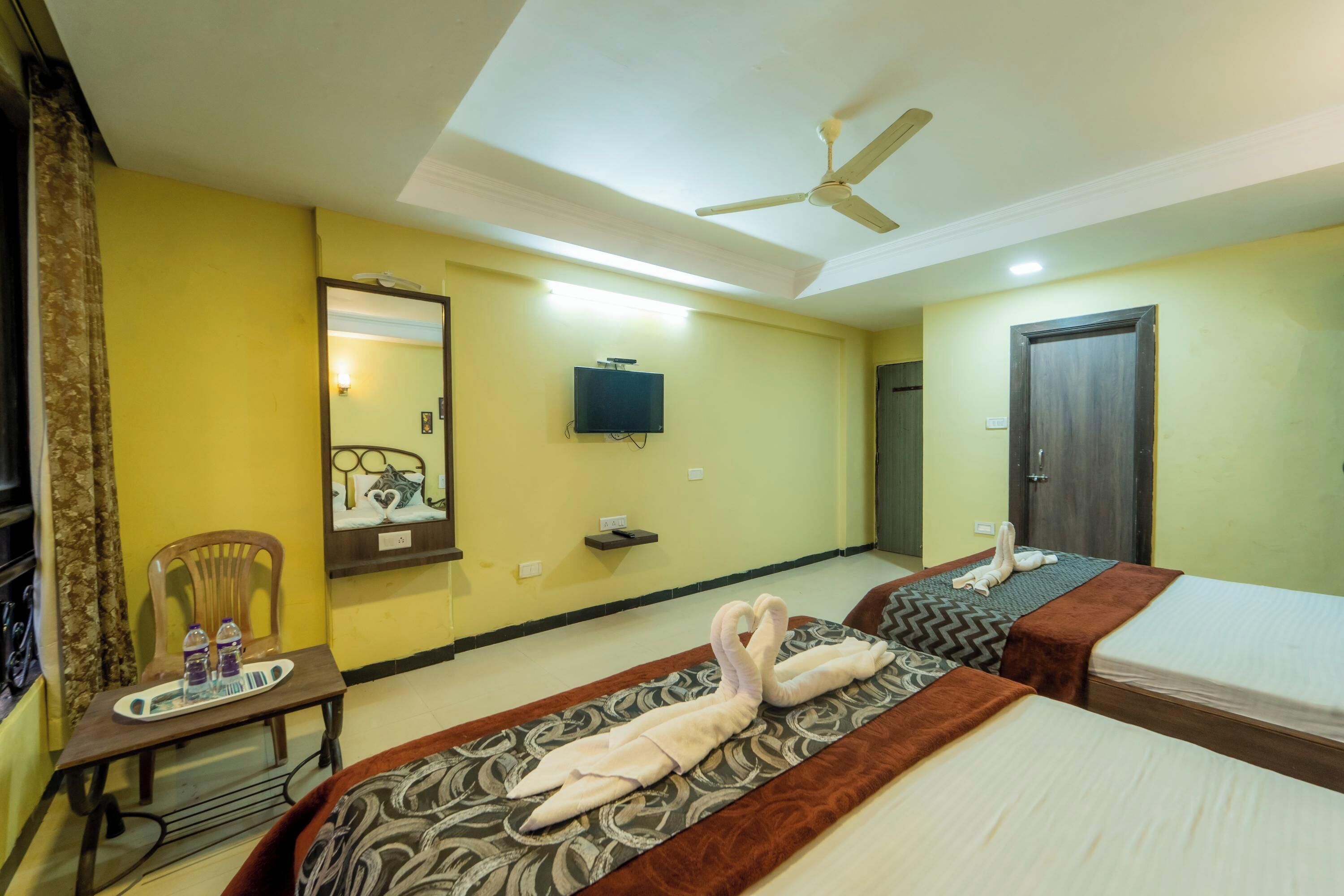A hotel room with two beds, a ceiling fan, a TV, and a small table with water bottles.