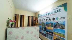 A hotel reception area with a floral-patterned counter, a poster advertising the hotel and its location, and a telephone. - Indira Nature Valley (Mahabaleshwar)