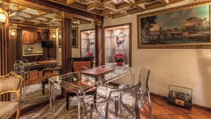 A dining area with a glass table and chairs, wooden ceiling beams, and a painting on the wall. - Campo de Fiori - Eleanor Suite luxury & history 1BD 1BH (Roma)