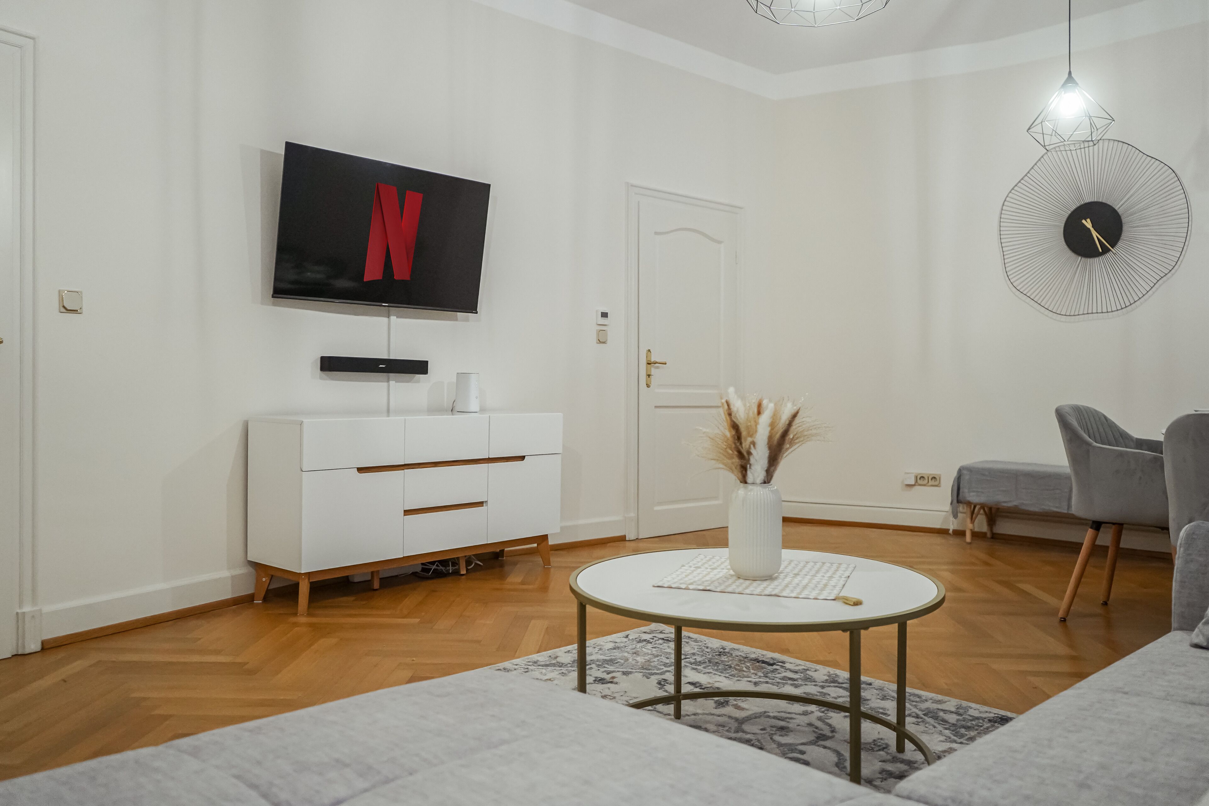A modern living room with a flat-screen TV displaying the Netflix logo, a white cabinet, a round coffee table, and a gray armchair.