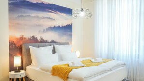 A neatly made bed with white linens and a yellow throw, a bedside lamp, and a wall mural of a mountainous landscape. - 7Seas Apartment Luxus-Altbau (Saarbrücken)