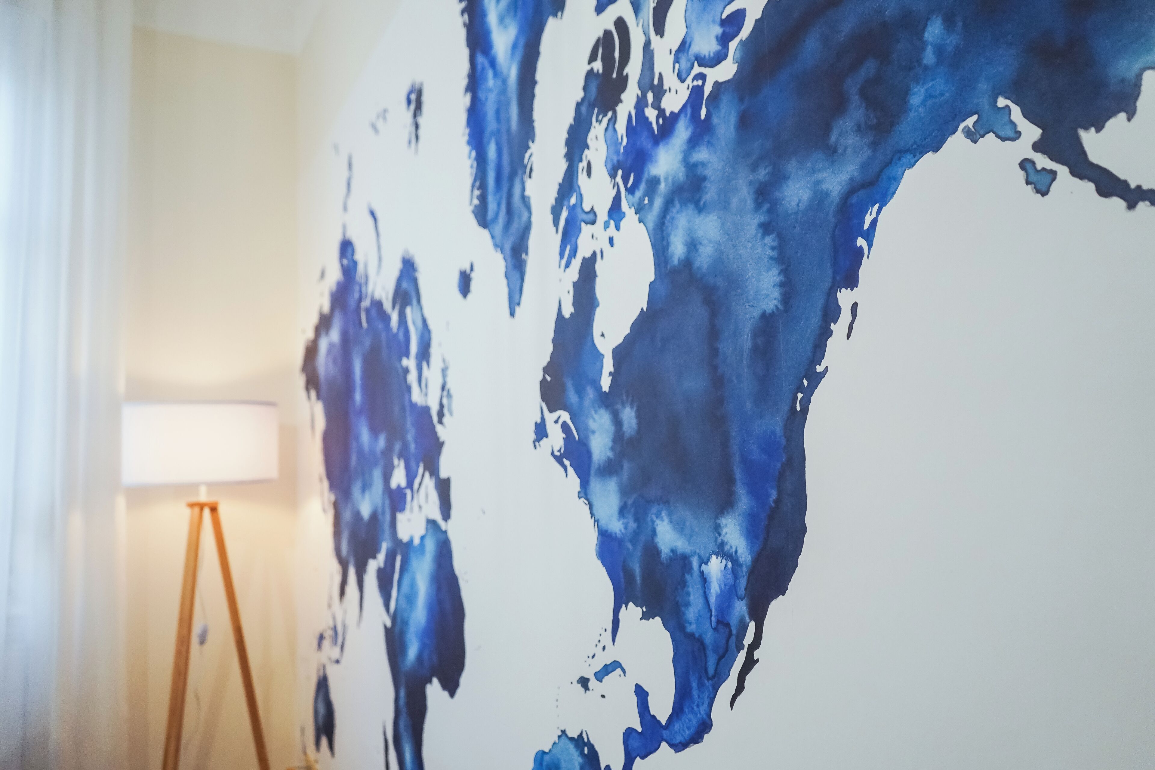 Een kamer met een groot abstract blauw kunstwerk aan de muur, een vloerlamp en een raam met gordijnen.