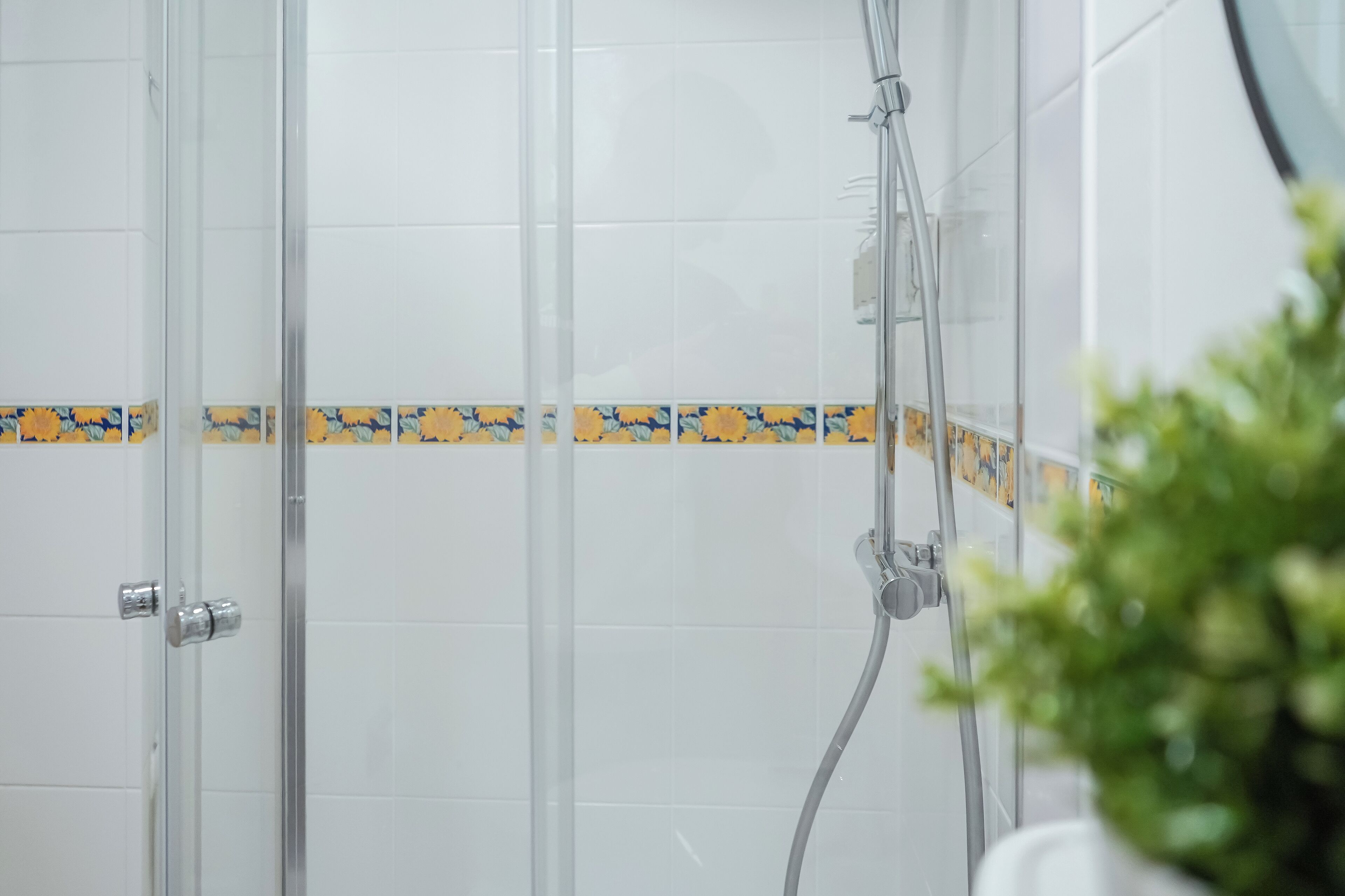 A shower area with glass doors and a tiled wall with a floral border.