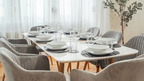 A dining table set with white plates, glasses, and cutlery, surrounded by grey upholstered chairs. - 7Seas Apartment Luxus-Altbau (Saarbrücken)