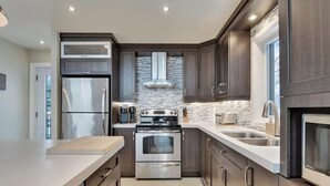 A modern kitchen with stainless steel appliances, dark wood cabinets, and a stone backsplash. - Manwë | Panoramique | Spa & Jeux by Alchalet (Petite-Rivière-Saint-François)