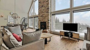 A spacious living room with a fireplace, large windows, and a television. - Manwë | Panoramique | Spa & Jeux by Alchalet (Petite-Rivière-Saint-François)