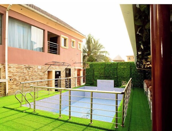 A residential property with a swimming pool, stone wall, and a well-maintained lawn. - House 27 (Lagos)