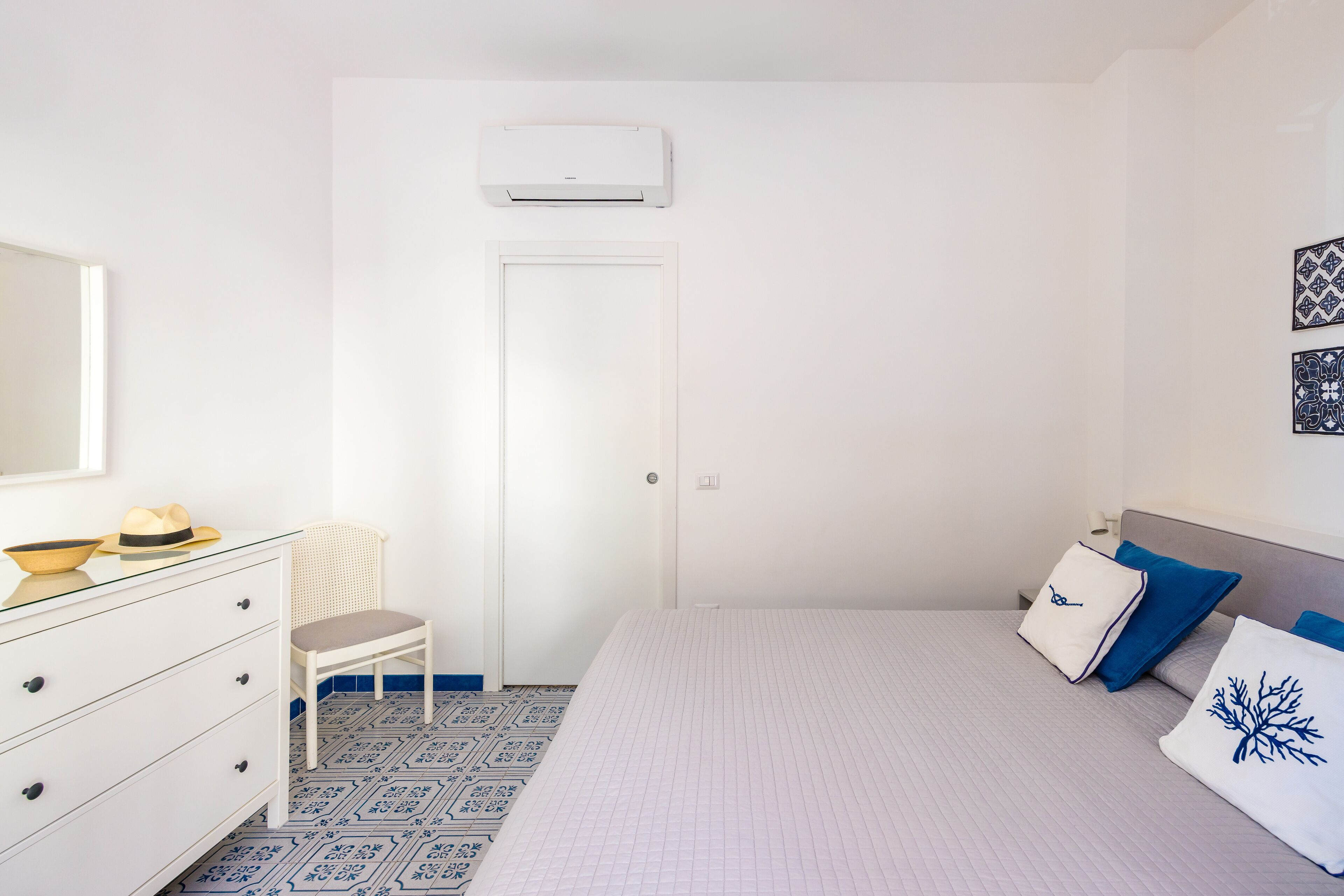 A bedroom with a bed, a dresser, a chair, a door, and an air conditioning unit.
