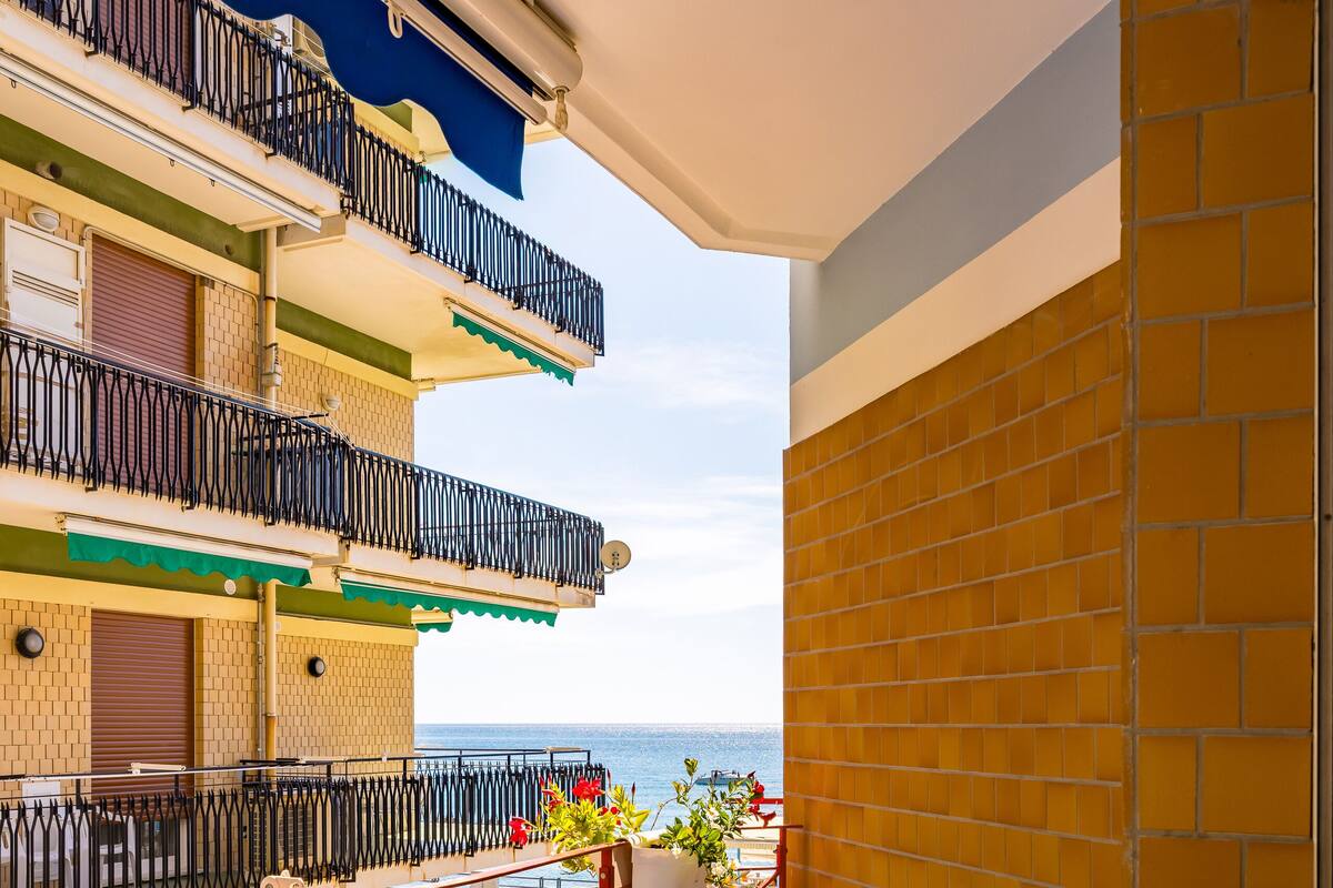 Un balcone con un tavolo apparecchiato per mangiare, una pianta in vaso e vista sul mare.