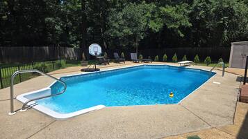 A rectangular swimming pool with a diving board and a basketball hoop.