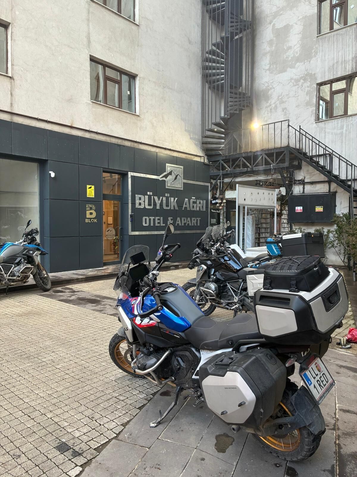 Uma motocicleta estacionada em frente a um edifício com uma placa que diz 'BUYUK AGRI OTEL & APART'.