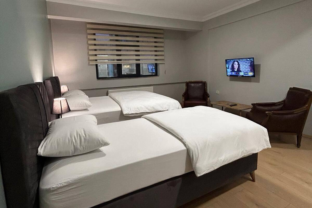 A modern bedroom with a large bed, a TV on the wall, and a window with blinds.