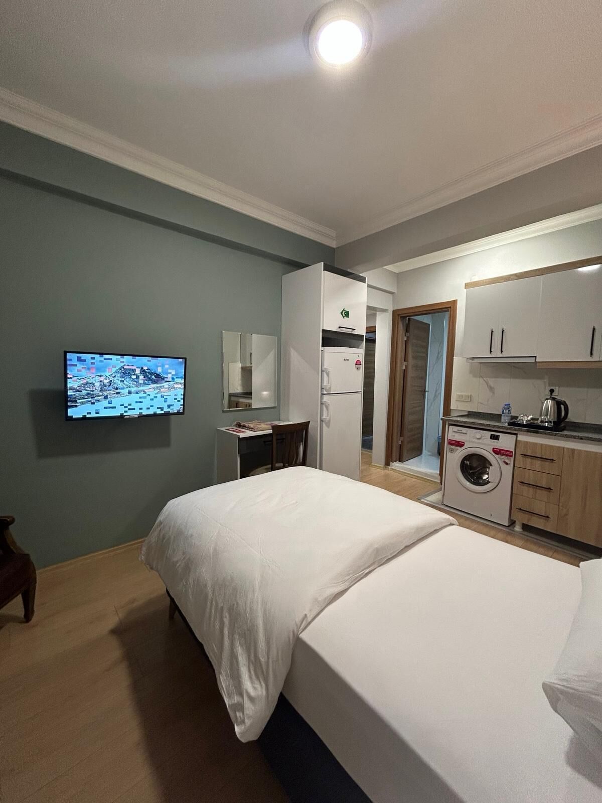 Hotelkamer met een bed, bureau, wasmachine, televisie en kitchenette.