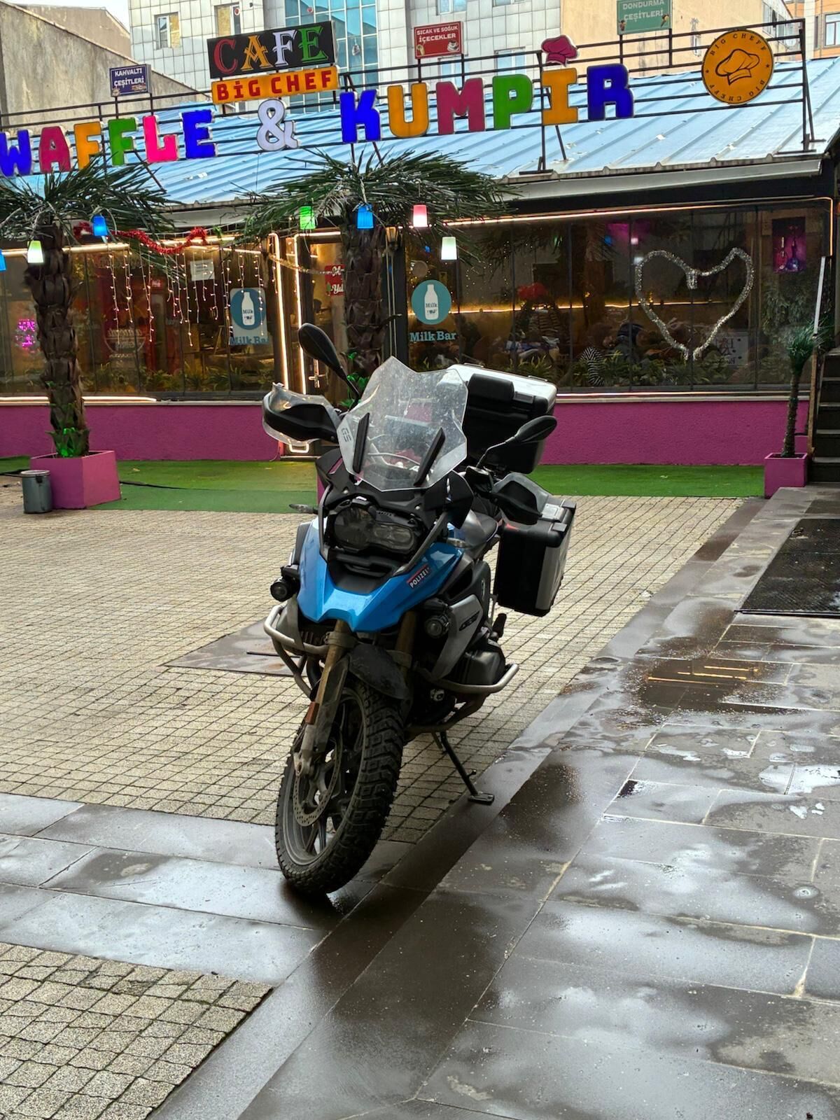 Une moto bleue est garée devant un bâtiment sur lequel on peut lire l’inscription « WAFFLE & KUMPTA ».