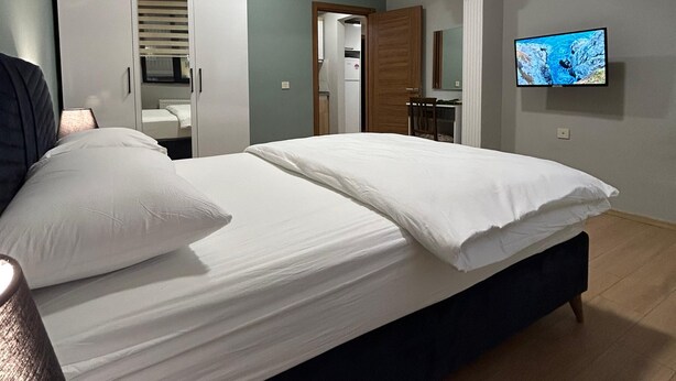 Une chambre à coucher avec un lit, un téléviseur fixé au mur et une salle de bain visible à travers une porte ouverte.