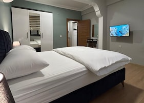 Un dormitorio con una cama, un televisor en la pared y un baño visible a través de una puerta abierta.