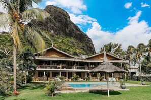 A resort with a pool, thatched-roof structures, and a mountain backdrop.