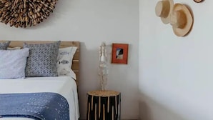 A bedroom with a bed, a round wall hanging, a small stool, and a framed picture. - Boutik Le Morne Holiday Apartments (Le Morne)