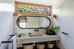 Een badkamer met een grote spiegel, een wastafel en een klein raam met uitzicht op groen.