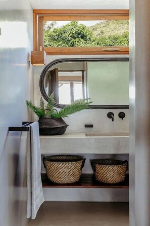 A compact bathroom with a window, a sink, a mirror, and two woven baskets on a shelf.