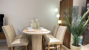 A dining area with a round table set for four, surrounded by upholstered chairs. There are decorative items on the table, and a potted plant is visible to the side. - Mynt stay hotel apartment - zed towers (Sheikh Zayed City)