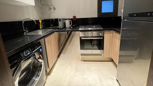A compact kitchen with a washing machine, a stove, and a microwave. - Mynt stay hotel apartment - zed towers (Sheikh Zayed City)