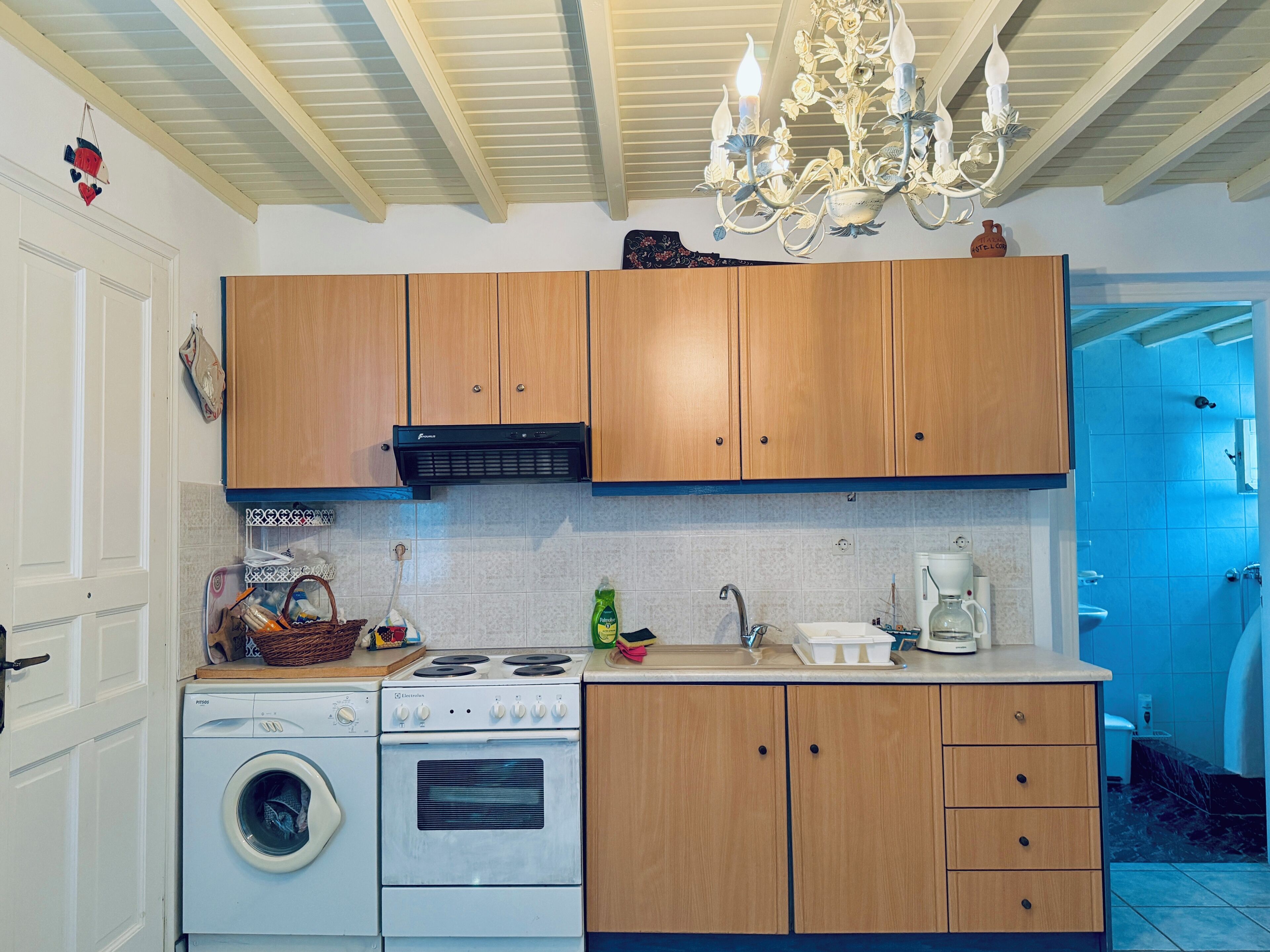 A kitchen with wooden cabinets, a washing machine, an electric stove, and a chandelier.