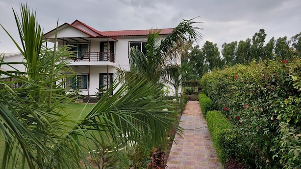 A two-story building with a red roof and a paved pathway leading to the entrance. - Luxsugero Farms (Faridabad)