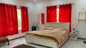 A bedroom with a bed, red curtains, a wooden headboard, a bedside table with a lamp, and a small stool. - Luxsugero Farms (Faridabad)