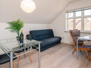 A modern living room with a glass dining table, a blue sofa, a wooden chair, a potted plant, and a bottle of wine. - 2 Person Holiday Home in Ringkobing (Ringkobing)