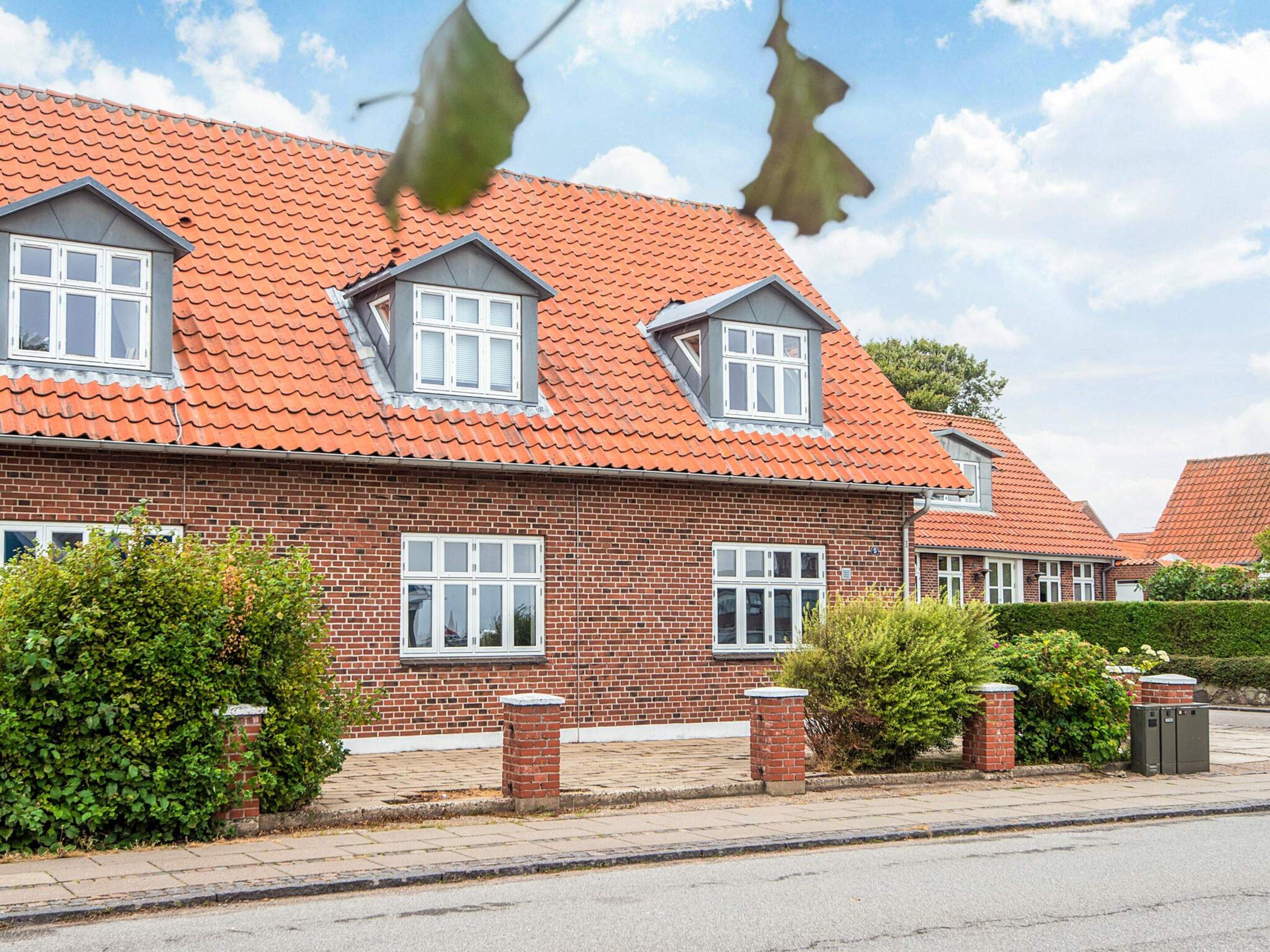A two-story brick house with a red-tiled roof, multiple windows, and a paved driveway.