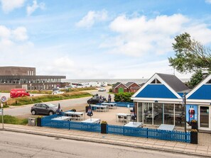A coastal area with a blue-roofed building, outdoor seating, and a parking lot. - 2 Person Holiday Home in Ringkobing (Ringkobing)