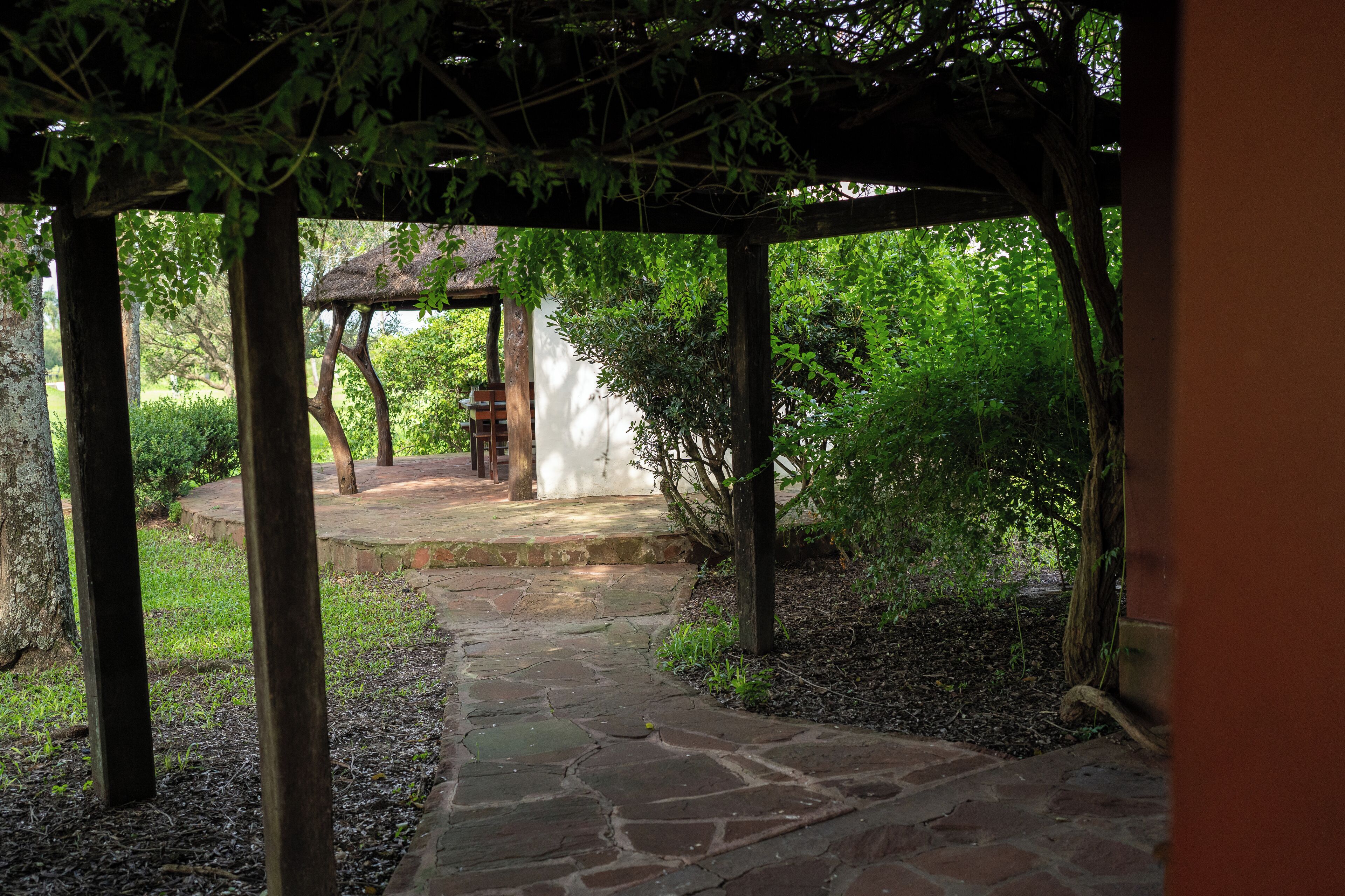 Un sendero de piedra conduce a un gazebo de madera con techo de paja, rodeado de exuberante vegetación.