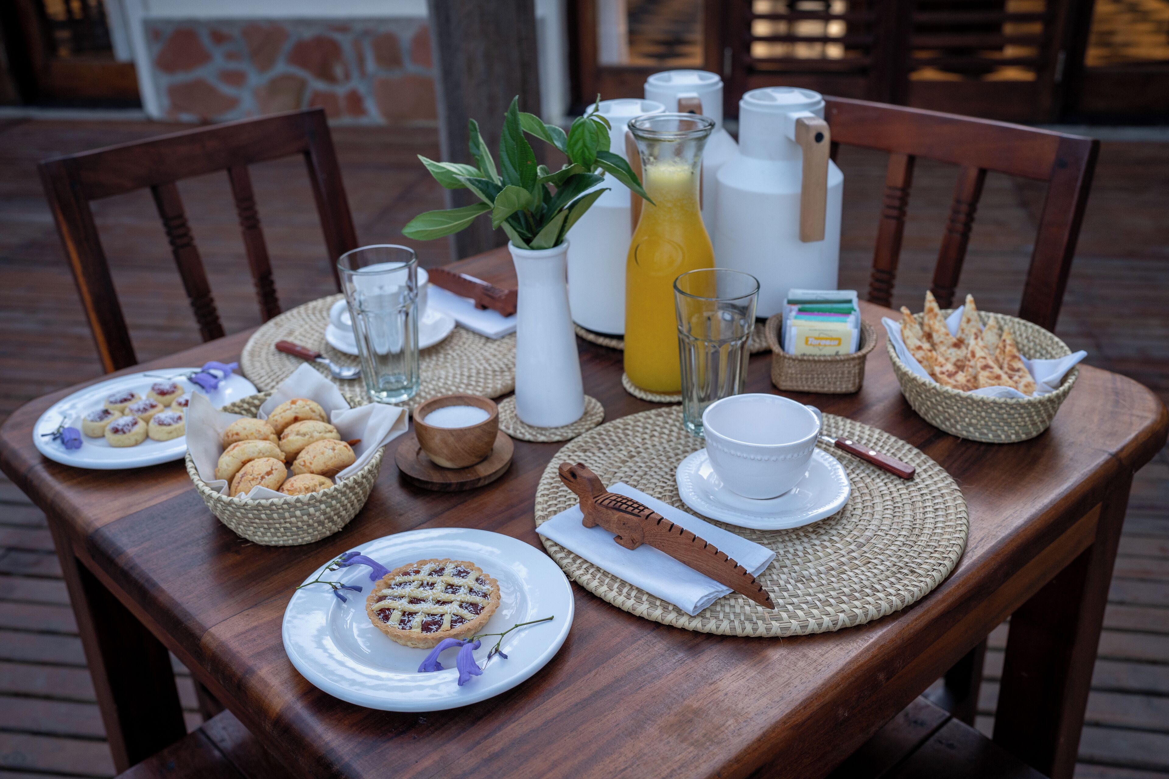 Una mesa de madera dispuesta con platos de comida, un jarro de jugo de naranja y diversos condimentos.