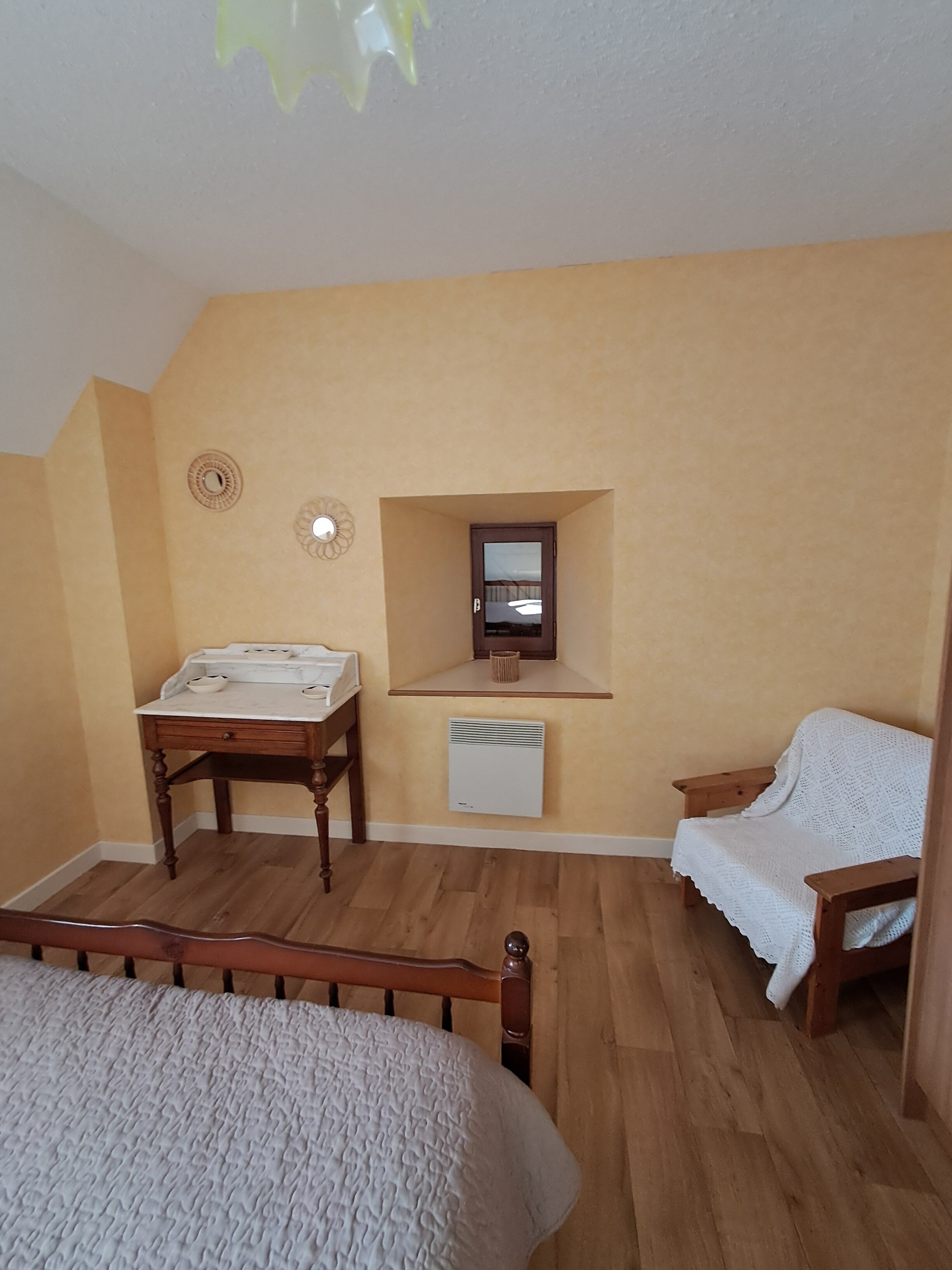 Une chambre avec un lit en bois, une table de chevet en bois, un petit bureau, une étagère intégrée avec un miroir et un radiateur blanc.