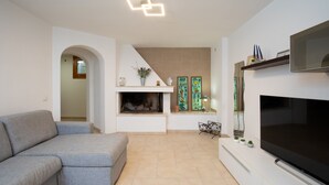 A modern living room with a grey sectional sofa, a flat-screen TV, a fireplace, and decorative wall art. - Casa Al Borgo by Wonderful Italy (Olbia)