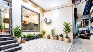 A hotel entrance with a tiled patio, potted plants, a large window, and a parked car. -  Atlas Inn Near to IGI Airport (Firoj)