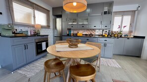 Uma cozinha moderna com armários cinza, uma mesa de madeira redonda com banquetas e um lustre pendente.