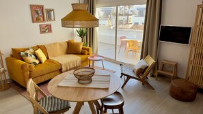 Uma sala de estar com um sofá amarelo, uma mesa de madeira redonda e uma televisão.