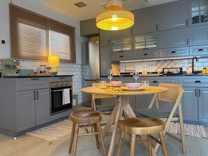 Uma cozinha moderna com armários cinza, uma mesa redonda de madeira e dois banquinhos de madeira.
