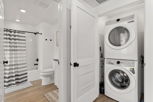 A modern bathroom with a shower, toilet, and stacked washer and dryer.
