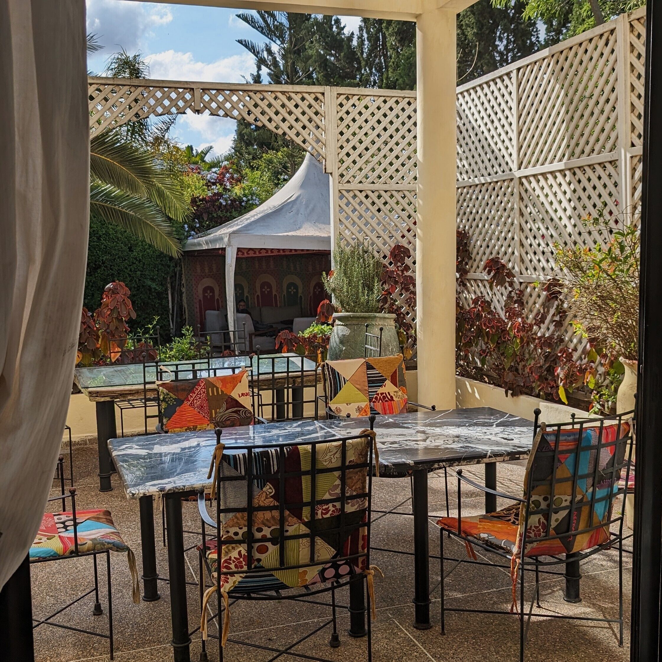 Un patio al aire libre con mesas y sillas, una cerca decorativa y vistas a un edificio con arcos.